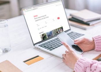 Pessoa utilizando celular e laptop em Airbnb - Créditos: depositphotos.com / VitalikRadko