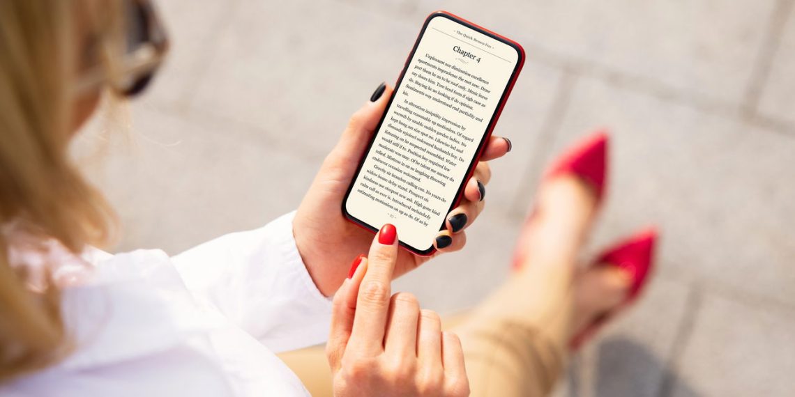 Moça lendo livro no iPhone - Créditos: depositphotos.com / grinvalds