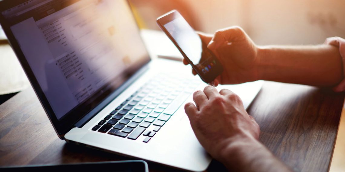 Homem usando celular e laptop - Créditos: depositphotos.com / GaudiLab