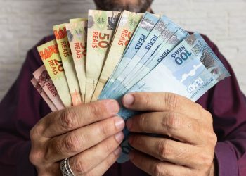 Homem segurando dinheiro brasileiro nas mãos - Créditos: depositphotos.com / verganifotografia