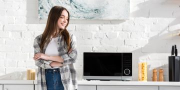 Mulher ao lado de micro-ondas - Créditos: depositphotos.com / HayDmitriy