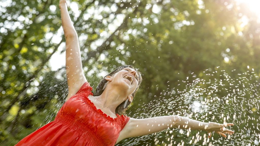 Mulher feliz tomando banho de mangueira - Créditos: depositphotos.com / Gajus-Images