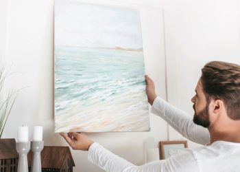 Homem colocando quadro na parede - Créditos: depositphotos.com / SashaKhalabuzar