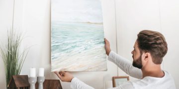 Homem colocando quadro na parede - Créditos: depositphotos.com / SashaKhalabuzar