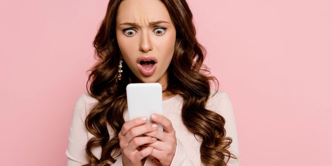 Mulher surpresa ao olhar notícia no celular - Créditos: depositphotos.com / IgorVetushko