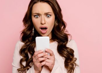 Mulher surpresa ao olhar notícia no celular - Créditos: depositphotos.com / IgorVetushko