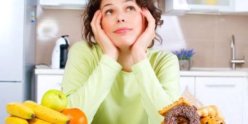 Mulher pensando entre comer vegetais e frutas ou comidas gordurosas - Créditos: depositphotos.com / Subbotina