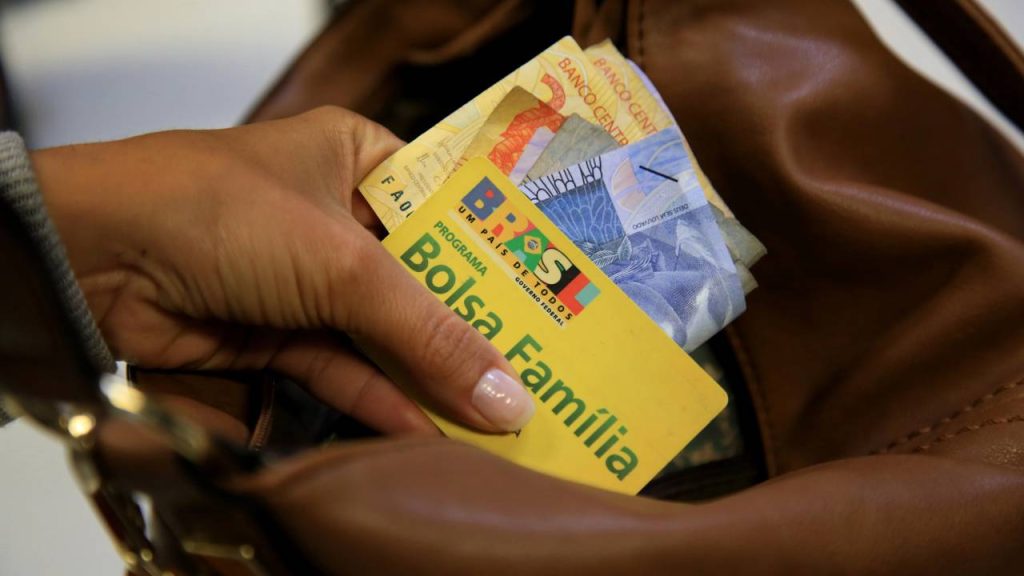 Cartão do Bolsa Família e dinheiro na mão - Créditos: depositphotos.com / joasouza