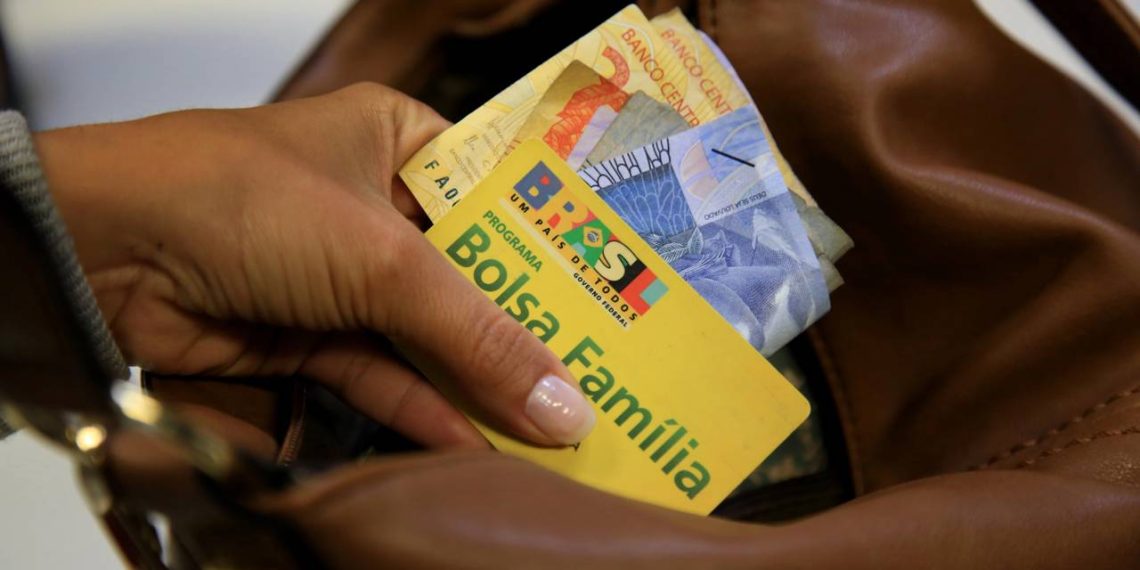 Cartão do Bolsa Família e dinheiro na mão - Créditos: depositphotos.com / joasouza