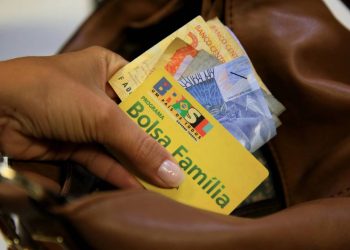 Cartão do Bolsa Família e dinheiro na mão - Créditos: depositphotos.com / joasouza