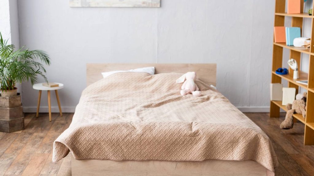 Quarto com parede cinza claro e cama com lençóis com tons de bege - Créditos: depositphotos.com / AndrewLozovyi