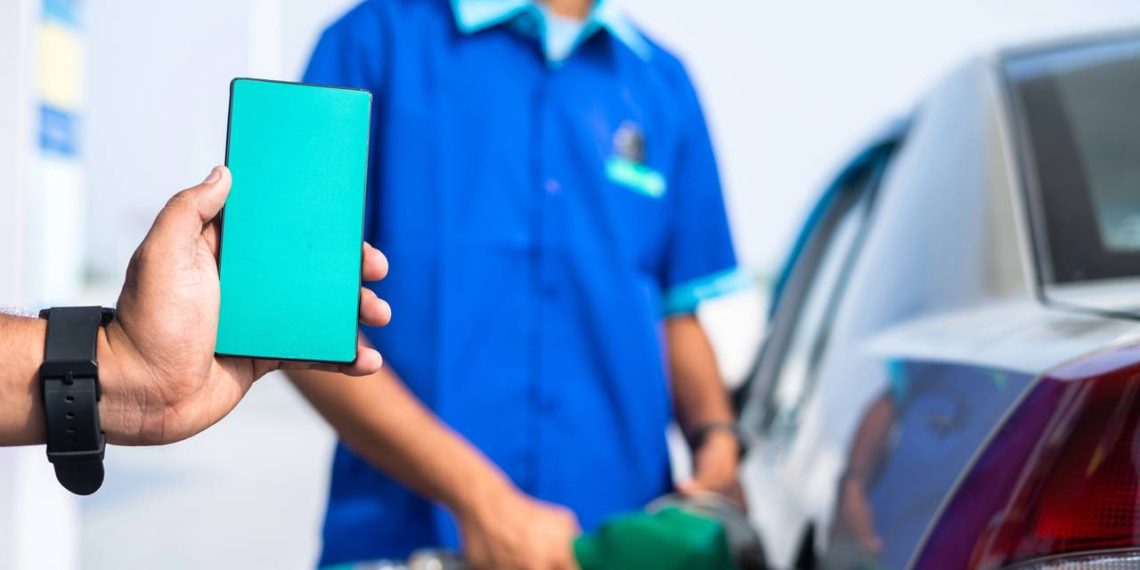 Homem segurando celular em posto de combustível - Créditos: depositphotos.com / Lakshmiprasad