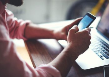 Homem utilizando celular e laptop – Créditos: Créditos: depositphotos.com / GaudiLab