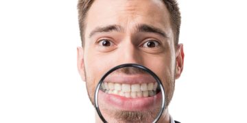 Homem com lupa na frente da boca - Créditos: depositphotos.com / EdZbarzhyvetsky