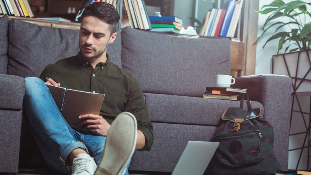 Aluno estudando escrevendo em caderno e com laptop ao lado - Créditos: depositphotos.com / alebloshka