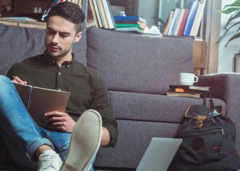 Aluno estudando escrevendo em caderno e com laptop ao lado - Créditos: depositphotos.com / alebloshka