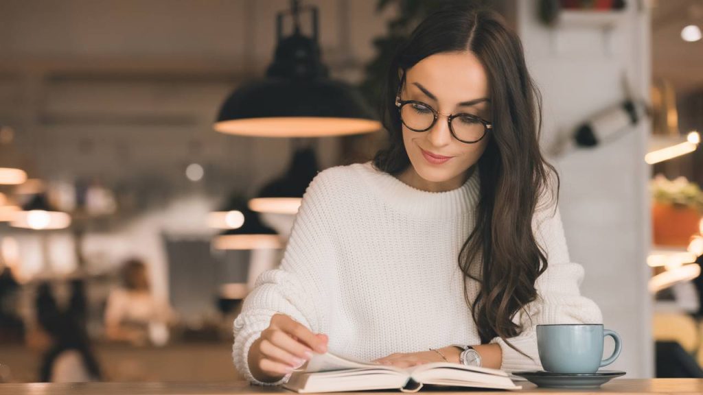 Mulher lendo em cafeteria - Créditos: depositphotos.com / AllaSerebrina