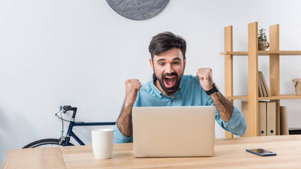 Homem recebendo boa notícia no laptop - Créditos: depositphotos.com / EdZbarzhyvetsky