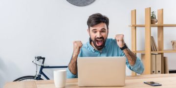 Homem recebendo boa notícia no laptop - Créditos: depositphotos.com / EdZbarzhyvetsky
