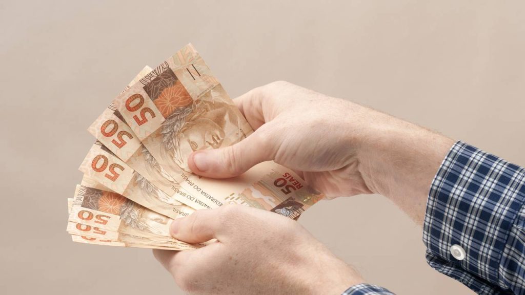 Homem com notas de 50 reais na mão - Créditos: depositphotos.com / rodrigobellizzi