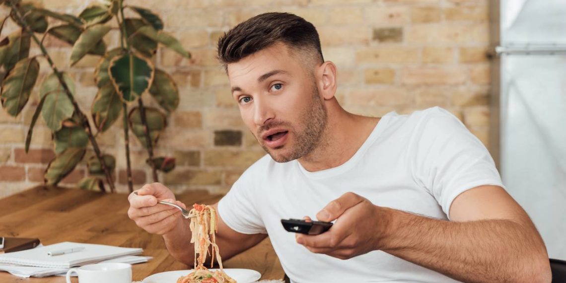 Homem assistindo TV e almoçando - Créditos: depositphotos.com / IgorVetushko