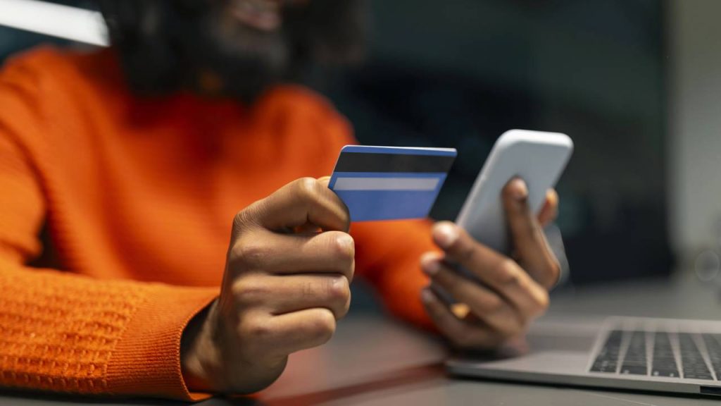 Homem com cartão e celular na mão - Créditos: depositphotos.com / Milkos