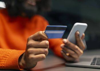 Homem com cartão e celular na mão - Créditos: depositphotos.com / Milkos