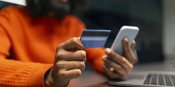 Homem com cartão e celular na mão - Créditos: depositphotos.com / Milkos