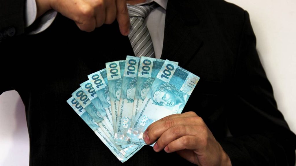 Homem segurando notas de cem reais - Créditos: depositphotos.com / joelfotos