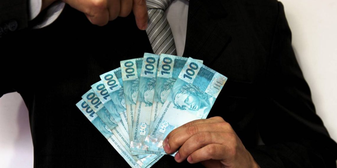 Homem segurando notas de cem reais - Créditos: depositphotos.com / joelfotos